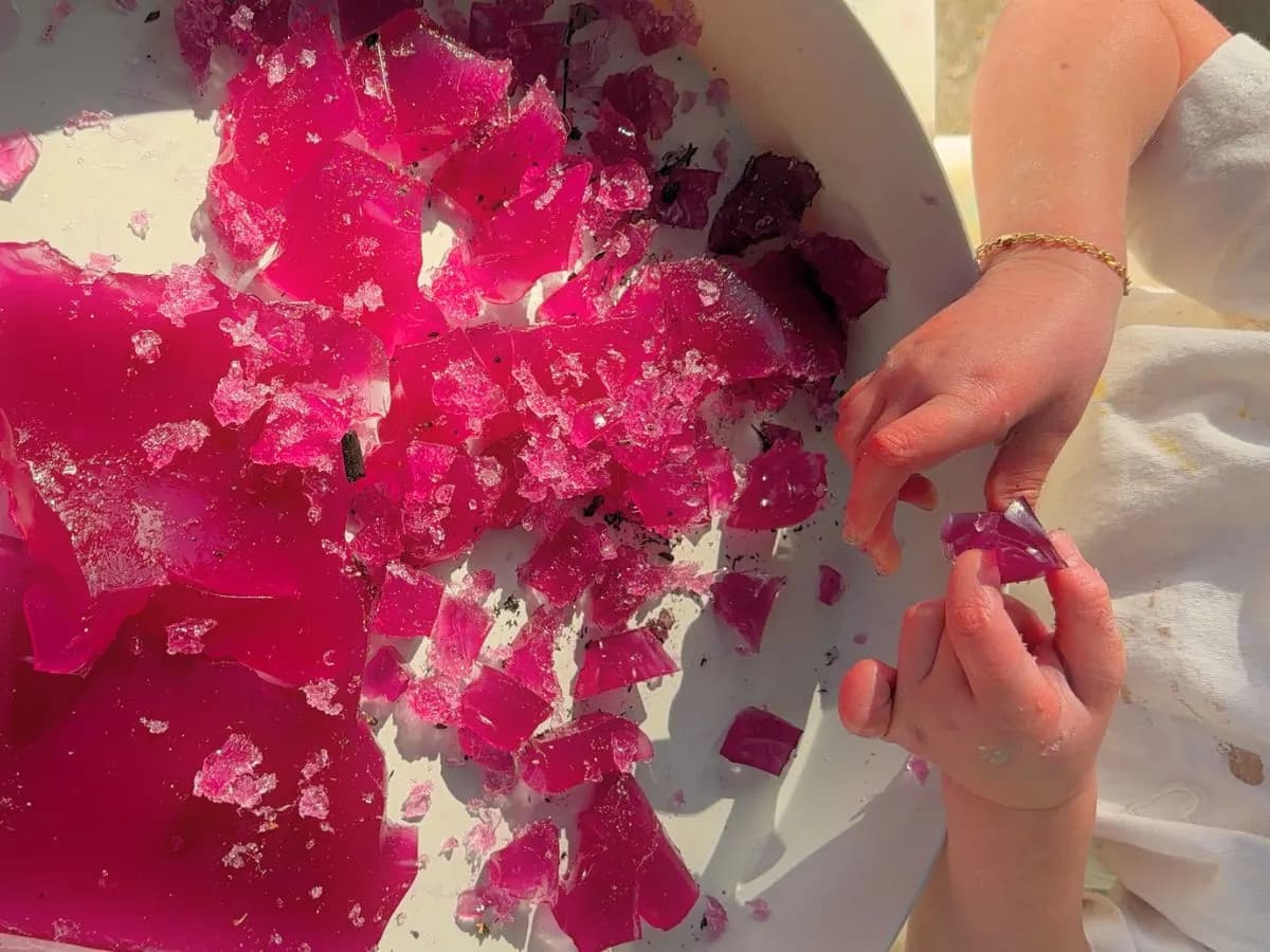 Small hands holding a piece of torn pink jelly over a white tray in the sun