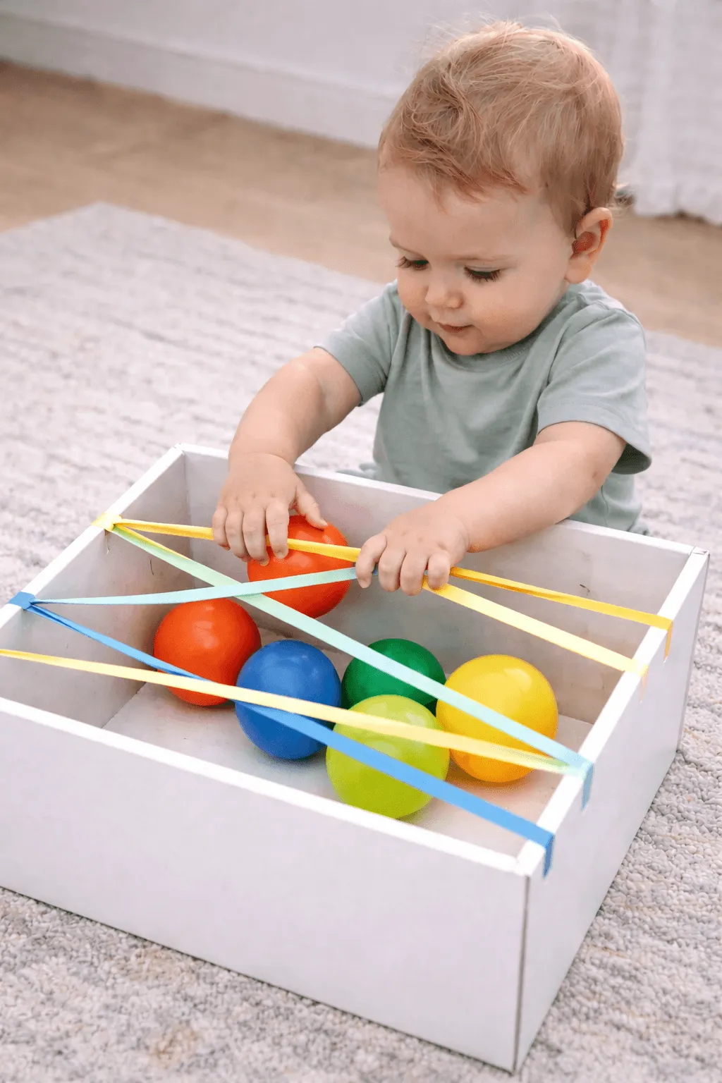 Toddler reaching through string stretched across a box to rescue colourful balls